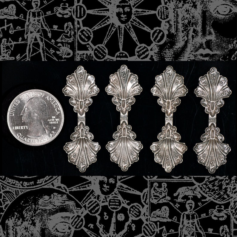 May include: Four silver spoon-shaped charms with a decorative scallop design. The charms are arranged in a row against a black background.