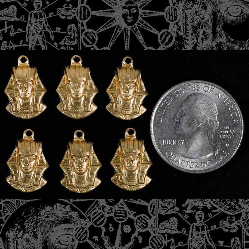 May include: Six gold-tone pendants featuring a profile of an Egyptian pharaoh with a headdress. The pendants are arranged in two rows of three. A US quarter dollar coin is included for scale.