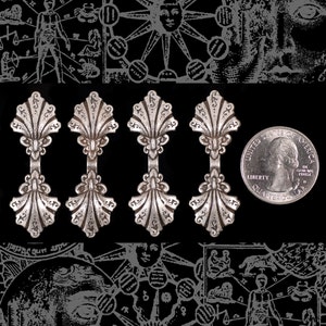 May include: Five silver-toned metal decorative pieces shaped like seashells with a scalloped edge. Each piece has a decorative design in the center and a loop at the top.
