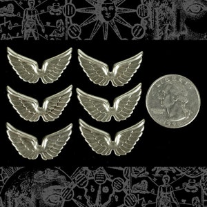 May include: Six silver angel wings charms, each with a slightly different design. The charms are about the size of a US quarter.