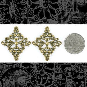 Peut inclure: Deux pièces décoratives en métal doré avec des motifs de filigrane complexes. Chaque pièce est en forme de diamant et présente une croix centrale avec des détails ornés. Les pièces sont approximativement de la taille d'une pièce de 25 centimes d'euro.