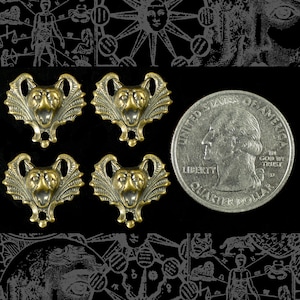 May include: Four antique brass-colored bat-like charms with detailed wings and faces, arranged near a US quarter for size comparison. The charms have a vintage aesthetic, perfect for jewelry making or crafting projects. The background is black with occult-themed illustrations.