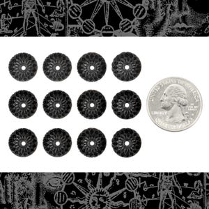 Może przedstawiać: Kolekcja dwunastu czarnych, rzeźbionych, okrągłych koralików z kwiatowym wzorem i centralnym otworem. Ćwierć dolara amerykańskiego jest dołączona do porównania rozmiarów. Koraliki są ułożone na białej powierzchni.