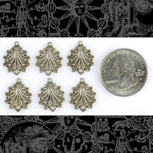 Puede incluir: Seis abalorios de metal plateado en forma de hojas estilizadas con dos agujeros para sujetar a joyas u otras manualidades. Los abalorios son aproximadamente del tamaño de una moneda de 25 centavos de dólar estadounidense.