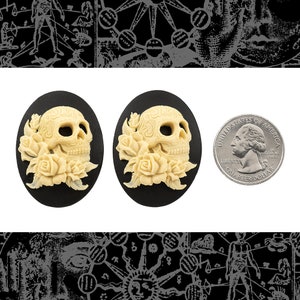 Puede incluir: Un par de pendientes ovalados de color negro y crema con forma de calavera y rosas. Los pendientes tienen un diseño detallado de calavera de azúcar con rosas. Los pendientes son aproximadamente del tamaño de una moneda de 25 centavos de dólar estadounidense.