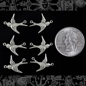 May include: Six silver-coloured bird charms with open jump rings for jewellery making. A US quarter is included for size reference. The charms are on a black background with a decorative border.