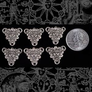 May include: Six silver-toned metal flower-shaped charms with three loops on each charm. The charms are arranged in two rows of three. A US quarter dollar coin is included for size comparison.