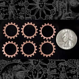 May include: Six copper gears of varying sizes, arranged in two rows of three, on a black background. A silver US quarter is placed to the right of the gears for scale.