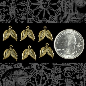 May include: Six antique gold-colored leaf charms with a quarter for size comparison. Each charm has a loop at the top for attaching to jewelry. The background is black with vintage illustrations.