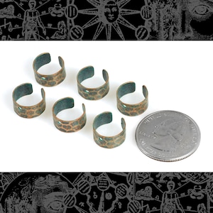 May include: Six copper-toned metal rings with a green patina and a hammered texture. The rings have a hole in the center and are approximately the size of a US quarter.