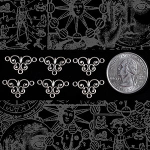 May include: Six silver-toned metal connector charms with a decorative scroll design. The charms are about the size of a US quarter.