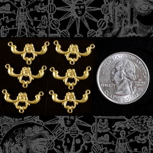 May include: Six gold-toned metal decorative embellishments with a floral design. Each embellishment has two loops on either end. The embellishments are arranged in two rows of three. A US quarter is included for scale.