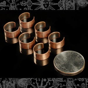 Puede incluir: Seis anillos de metal de color cobre con un acabado liso y ligeramente texturizado. Cada anillo tiene un pequeño agujero en el lateral. Se incluye una moneda de 25 centavos de dólar estadounidense como referencia de tamaño.
