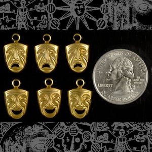 May include: Six gold-colored metal charms shaped like theatrical masks. Each mask has a different expression, including happy, sad, and surprised. The charms are arranged in two rows of three.