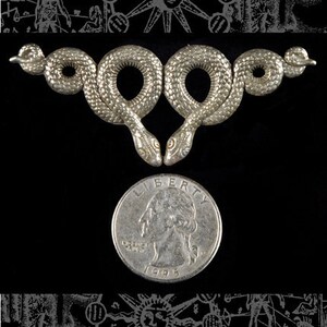 May include: Silver double snake pendant with a textured surface. The pendant is about the size of a quarter.
