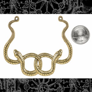 Peut inclure: Un collier doré représentant un motif de serpent. Le collier comporte deux têtes de serpent entrelacées. Le collier est à côté d'une pièce de monnaie pour référence de taille. Le fond a un motif noir et blanc.