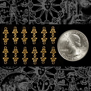 May include: A set of 10 gold-toned metal star charms with a loop at the top. Each charm has three stars connected together. The charms are arranged in three rows of three charms each, and one row of four charms.