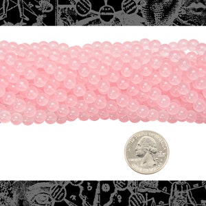 Peut inclure: Un brin de perles rondes rose p&acirc;le, d'environ 6 mm de diam&egrave;tre, avec une finition lisse et polie. Les perles sont dispos&eacute;es en une seule rang&eacute;e et sont photographi&eacute;es &agrave; c&ocirc;t&eacute; d'une pi&egrave;ce de 1 euro pour l'&eacute;chelle.