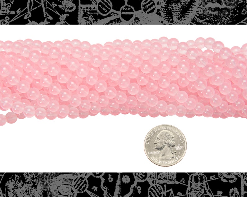 Peut inclure: Un brin de perles rondes rose p&acirc;le, d'environ 6 mm de diam&egrave;tre, avec une finition lisse et polie. Les perles sont dispos&eacute;es en une seule rang&eacute;e et sont photographi&eacute;es &agrave; c&ocirc;t&eacute; d'une pi&egrave;ce de 1 euro pour l'&eacute;chelle.