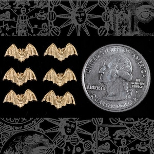 May include: Six gold-colored bat charms, each about the size of a US quarter, on a black background.