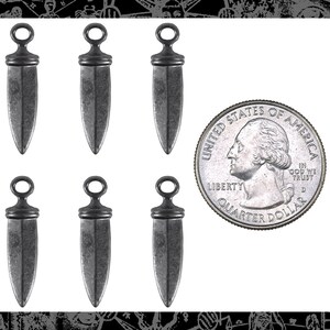 May include: Six silver-toned dagger-shaped charms with a loop at the top. The charms are about the size of a US quarter.