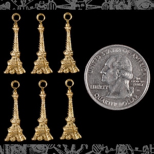May include: Six gold-colored Eiffel Tower charms with a loop at the top. The charms are about the size of a US quarter.