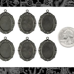 May include: Six silver-toned oval-shaped pendant frames with ornate edges. The frames are approximately the size of a US quarter.