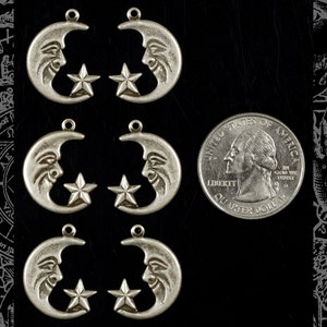 May include: Six silver-toned metal charms shaped like a crescent moon with a star inside. The charms have a face-like design on the moon. The charms are about the size of a US quarter.