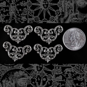 May include: Four silver-toned metal decorative embellishments in the shape of a stylized floral design. Each embellishment is about the size of a US quarter.