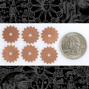 May include: Six copper-colored gear-shaped metal charms with a hole in the center. The charms are arranged in two rows of three. A US quarter is included for size comparison.