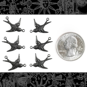 May include: Six silver-toned metal bird charms with a loop at the top. The charms are shaped like a swallow with outstretched wings. The charms are about the size of a UK 20 pence coin.