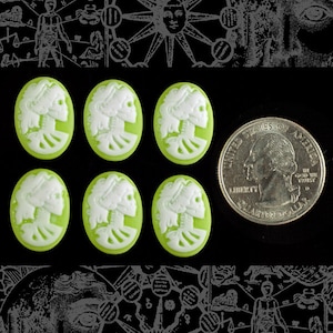 May include: Six green cameo-style buttons with a white design of two skeletons facing each other. The buttons are about the size of a US quarter.