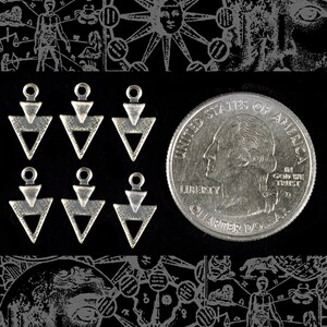 May include: Six silver triangle charms with a black background. The charms are in the shape of a triangle with a smaller triangle inside. A quarter dollar coin is also in the image.