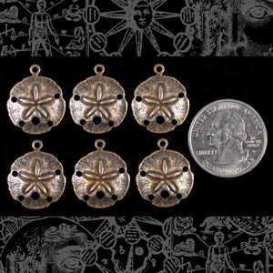 May include: Six antique gold-toned metal sand dollar charms with a starburst design. The charms are approximately the size of a US quarter.