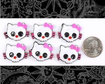 May include: Six white skull-shaped charms with pink bows. The charms are approximately 1 inch in diameter.