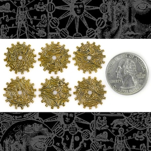 Op de afbeelding: Zes gouden metalen tandwielen met ingewikkelde ontwerpen. Elk tandwiel heeft een klein gaatje in het midden. De tandwielen zijn gerangschikt in twee rijen van drie. Een Amerikaanse kwartje is opgenomen voor schaal.