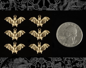 May include: Six gold-colored bat charms with a loop for hanging. The charms are arranged in two rows of three, with a silver US quarter dollar coin for scale.