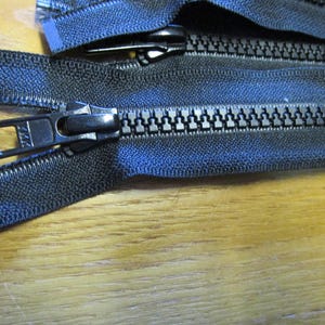 May include: Close-up of a black zipper with a black slider. The zipper is made of a durable nylon material and has a smooth, even finish.