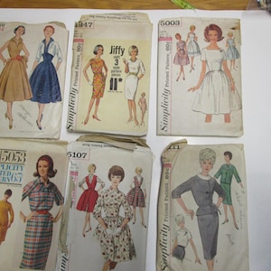 May include: Six vintage Simplicity sewing patterns for women's dresses and a skirt. The patterns are printed on paper and feature illustrations of the garments. The pattern numbers are 15053, 5107, 5003, 1847, and 1947.