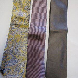 May include: Three neckties, one with a paisley pattern in yellow and blue, one with diagonal stripes in pink and blue, and one solid gray.