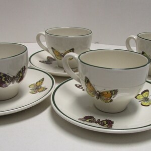 May include: Set of four white teacups and saucers with green trim. Each cup and saucer features a different butterfly design with yellow, brown, and black accents.
