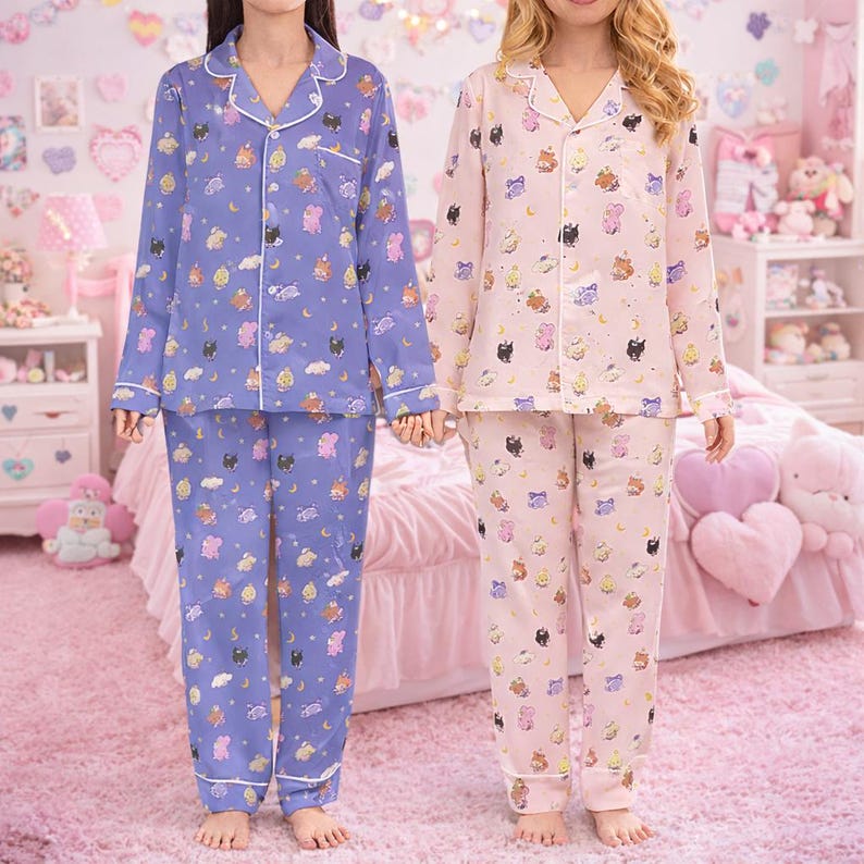 May include: Two sets of pajamas, one lavender and one pink, each with a button-down top and pants. The pajamas are patterned with cartoon characters, clouds, and moons. White trim accents the collar, cuffs, and pockets.