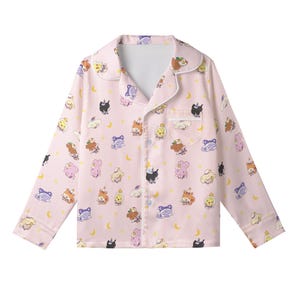May include: Pink pajama top with a repeating pattern of cartoon characters, moons, and stars. The long-sleeved top has a collared neckline, a chest pocket, and white trim. The pajama top is button-down.