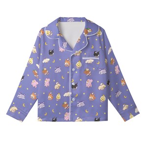 May include: A button-down pajama top in a periwinkle blue hue, adorned with a repeating pattern of cartoon characters, clouds, crescent moons, and stars. The pajamas have white trim and a chest pocket. The long-sleeved top is made of a soft, comfortable material.