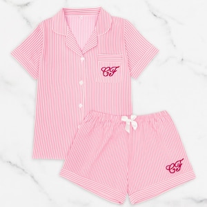 Puede incluir: Conjunto de pijama a rayas rosas y blancas. La parte superior de manga corta tiene un bolsillo en el pecho con iniciales bordadas. Los pantalones cortos a juego tienen un lazo blanco e iniciales bordadas. El conjunto está hecho de tela suave.
