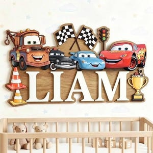 May include: A wooden wall sign featuring the name LIAM in large white letters. The design includes colorful cartoon cars, two checkered flags, a traffic light, a traffic cone, and a gold trophy. The characters are arranged above the name.