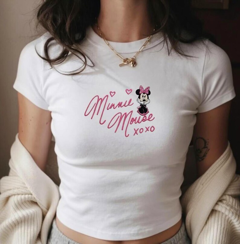 Pu&ograve; includere: T-shirt bianca a maniche corte con un design ricamato rosa. Il design presenta Minnie Mouse e il testo "Minnie Mouse xoxo", insieme a due cuori e un'immagine a cartoni animati di Minnie Mouse con un fiocco rosa.