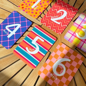 Puede incluir: Un conjunto de tarjetas de hitos para bebés numeradas del 1 al 6. Cada tarjeta presenta un diseño único, incluyendo lunares, zigzags, rayas, cuadros y un patrón de tablero de ajedrez. La palabra "mois" está impresa en cada tarjeta.