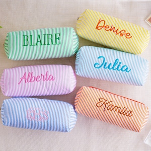 May include: Six personalised pencil cases in different colours, each with a name embroidered in a contrasting colour. The cases are striped and cylindrical, with names like "Blair" and "Denise".