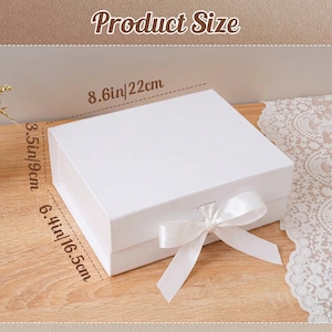 Peut inclure: Une bo&icirc;te cadeau blanche avec un n&oelig;ud en ruban de satin. La bo&icirc;te mesure 22 cm de large, 16,5 cm de long et 9 cm de haut. Le texte "Product Size" est en haut de l'image.
